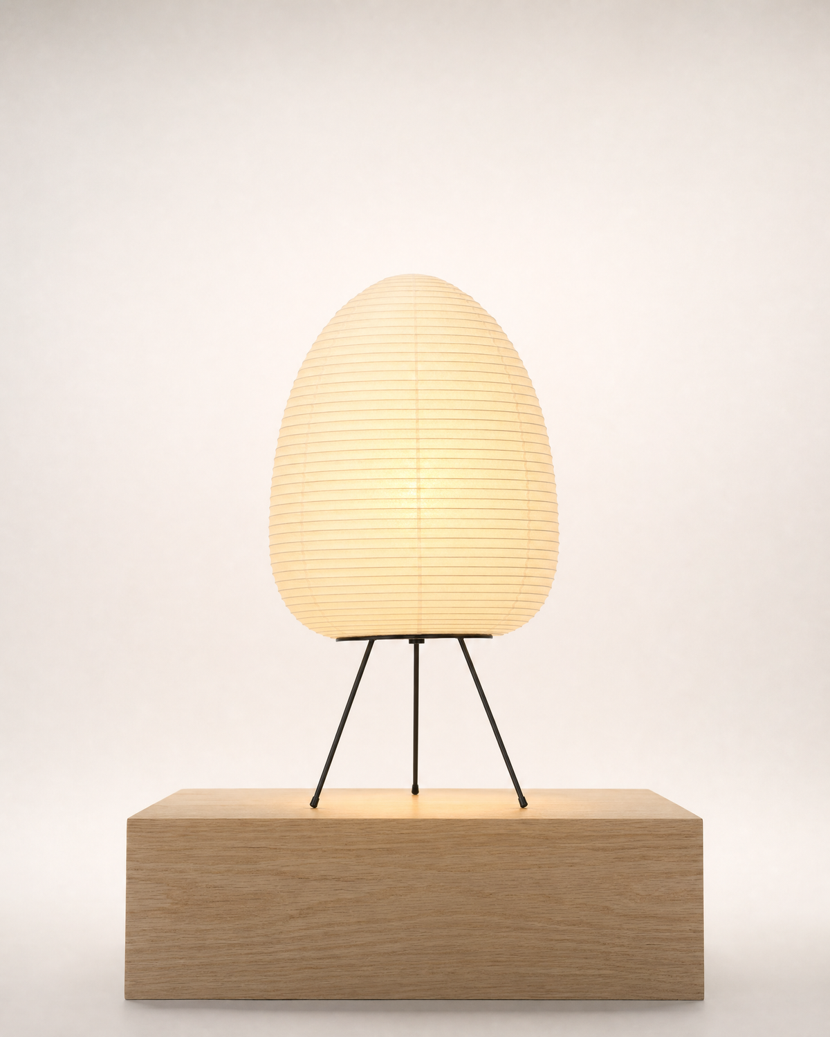 Rice paper table lamp on a black tripod, lit, on a pale oak block